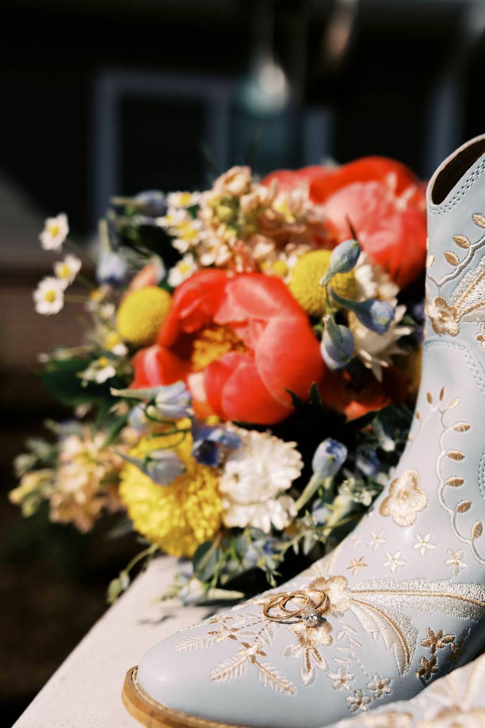 Elegant white bridal shoe decorated with floral embroidery and pearls displayed alongside colorful spring flowers.