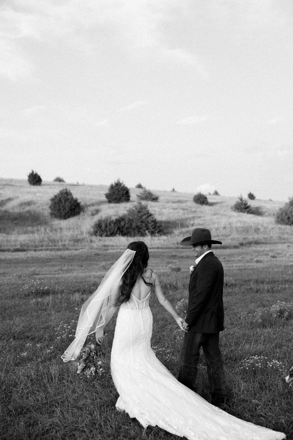 A dramatic wedding photo showing the bride's long train and veil against a rolling landscape.