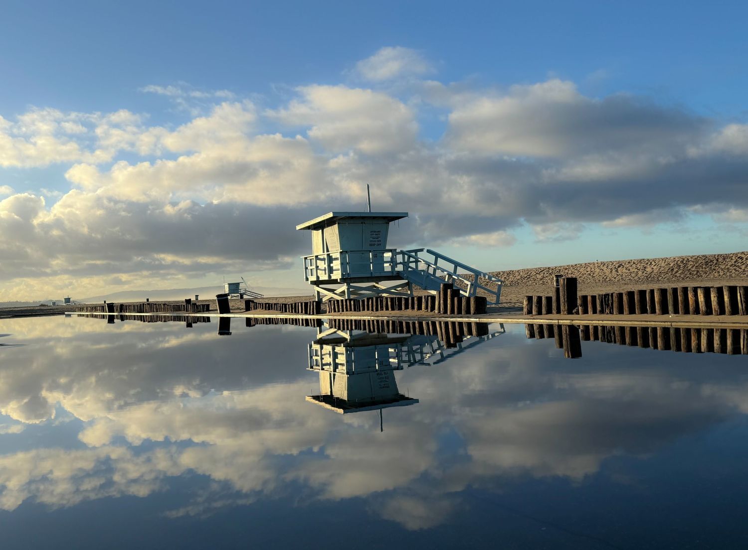 Panoramic view of pier with lifeguard tower reflecting in calm water at dusk.