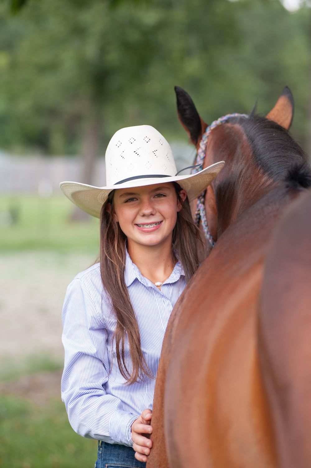 A close-up view of someone wearing a white cowboy hat interacting with a horse on a sunny day.