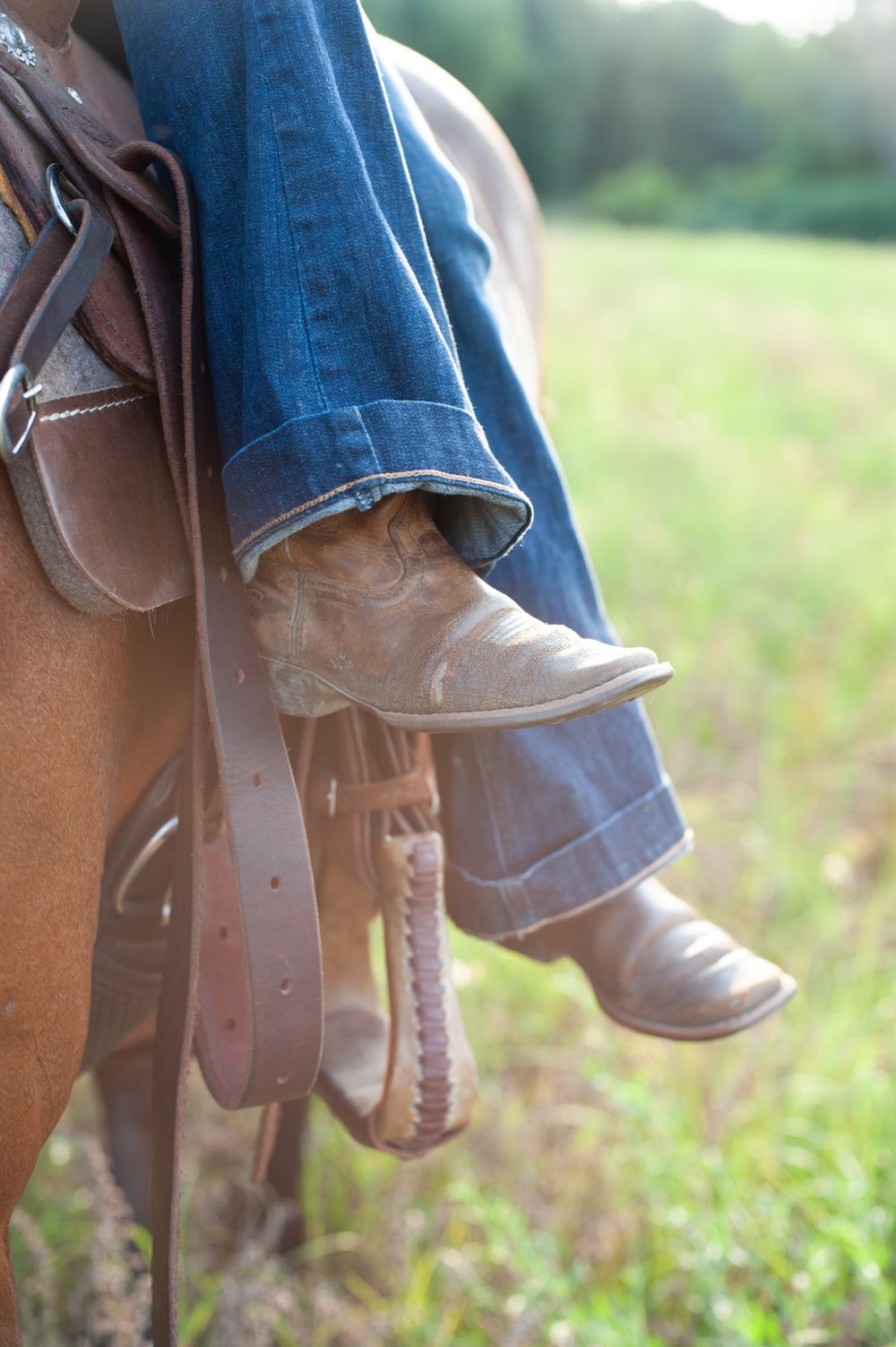 Close-up detail of worn cowboy boots and blue jeans while horseback riding.