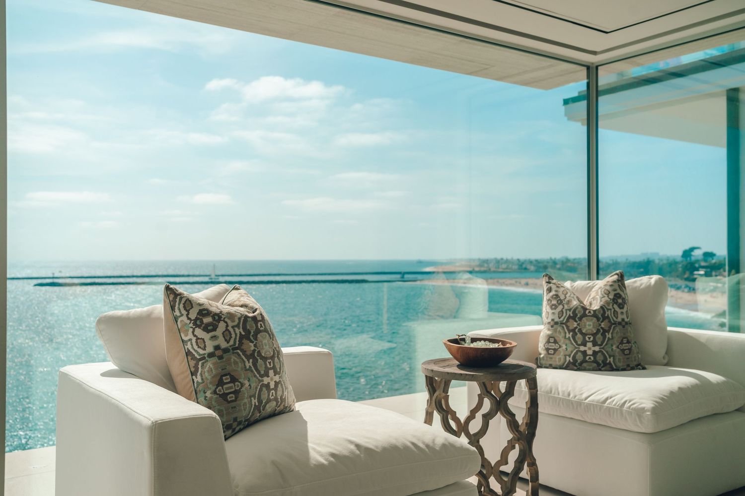 Modern luxury living room with floor-to-ceiling windows, beige sectional sofa, and pacific ocean  view through glass walls at corona del mar
