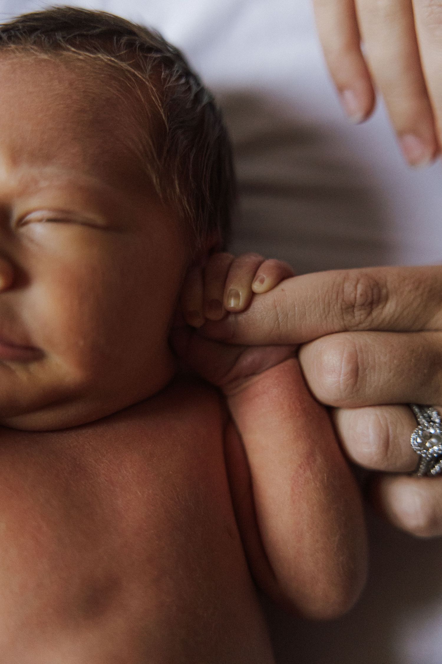 A close-up of a newborn baby having their ear folded by adult hands wearing a sparkly ring.