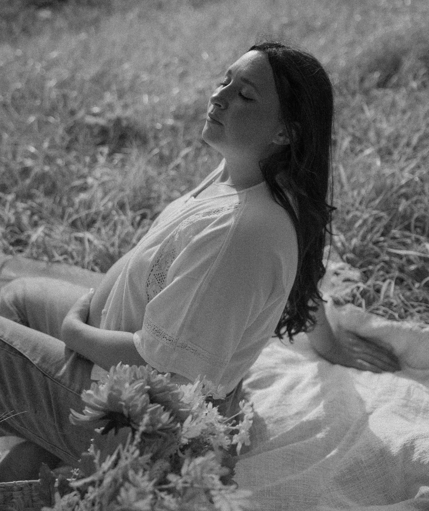 Person in a white dress lying in a grassy meadow while expressing serene emotion in black and white photography.