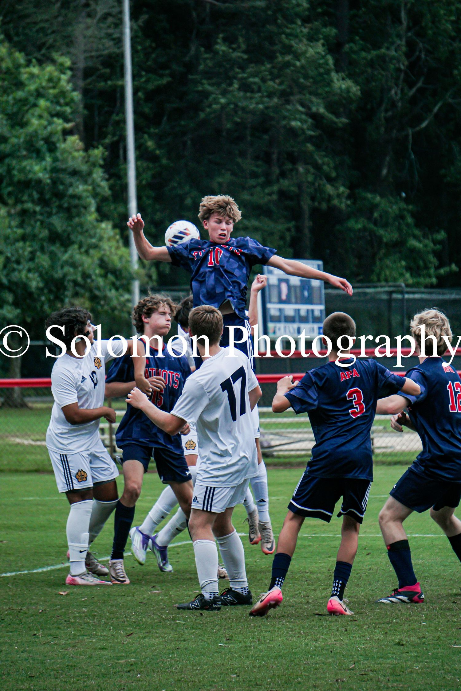 Soccer player leaps high to head ball during outdoor high school boys soccer match.