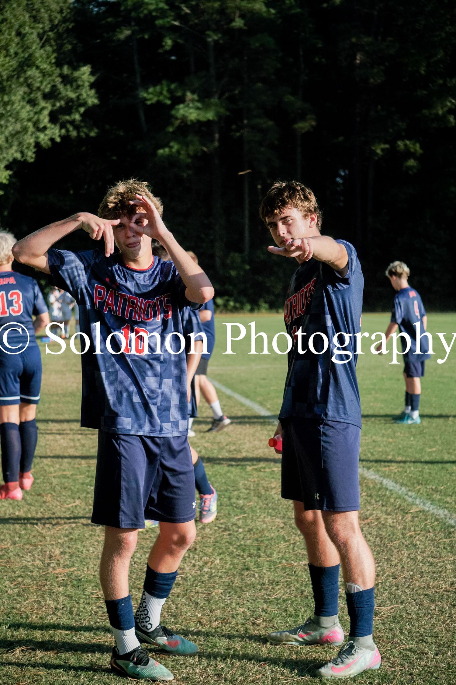 Two Patriot soccer players pose playfully on the field during a sunny game day.