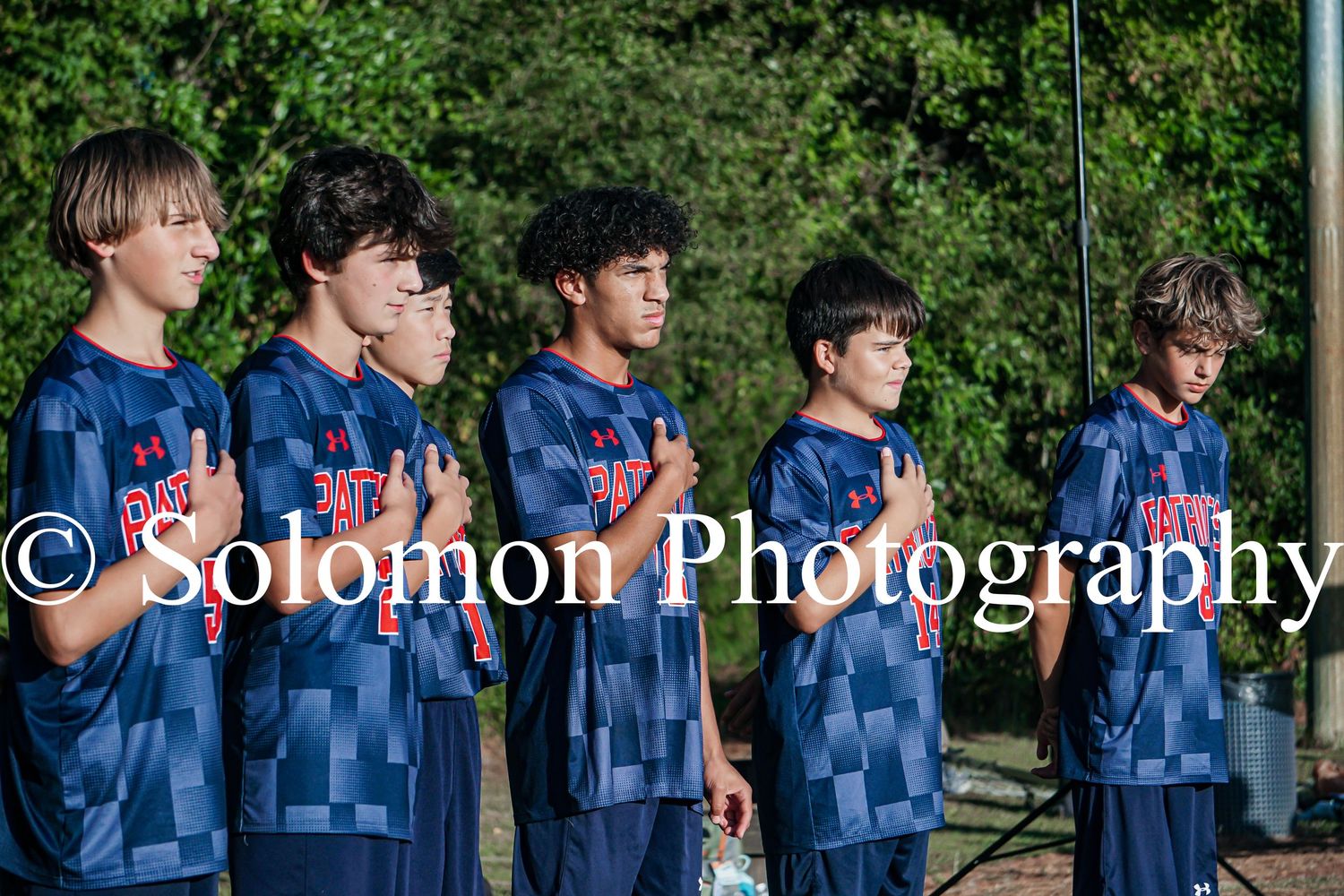Five Patriot soccer players stand at attention during the national anthem before a match.