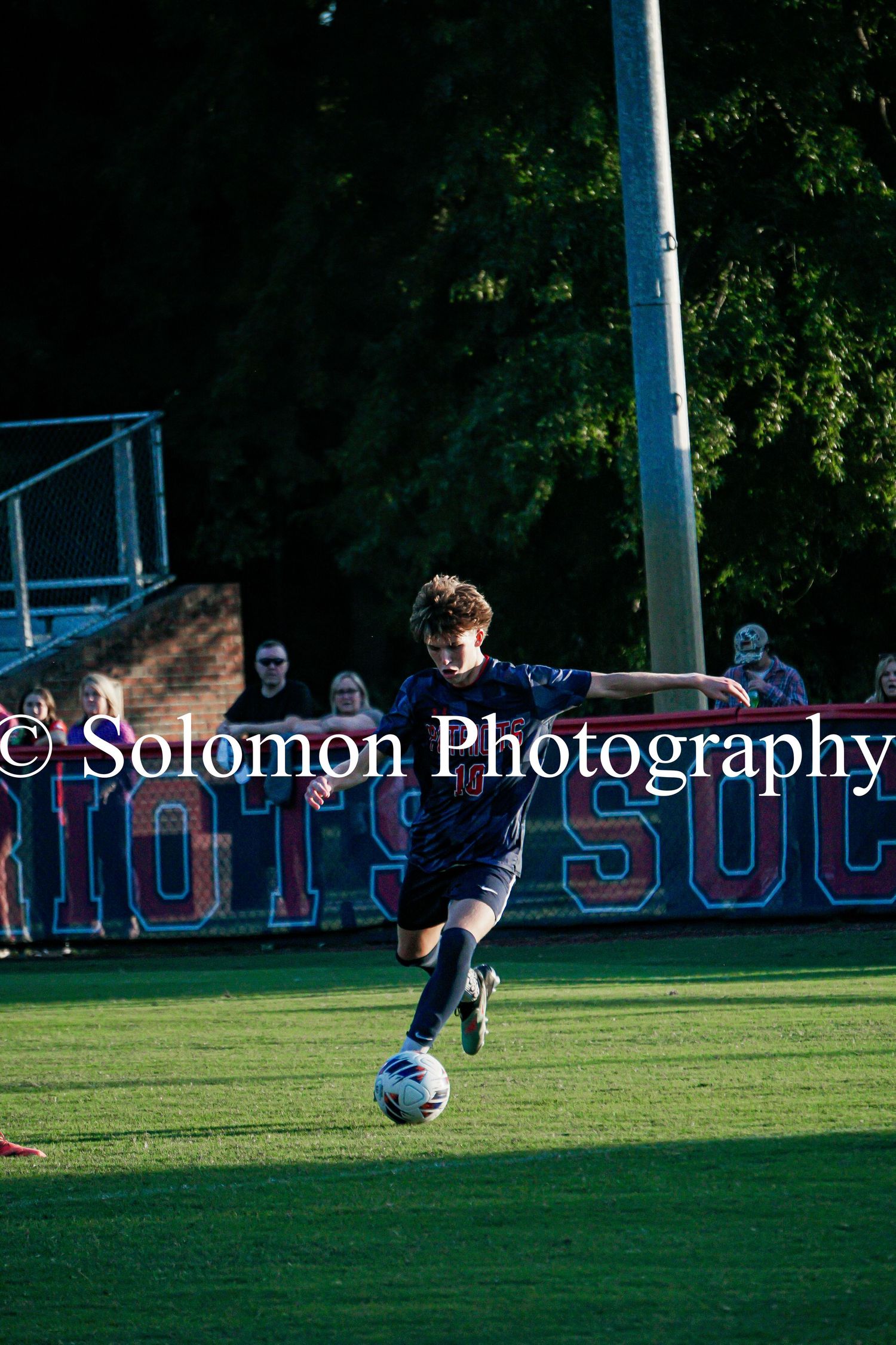 Patriot soccer player dribbles the ball down the field during an evening match by Solomon Photography.