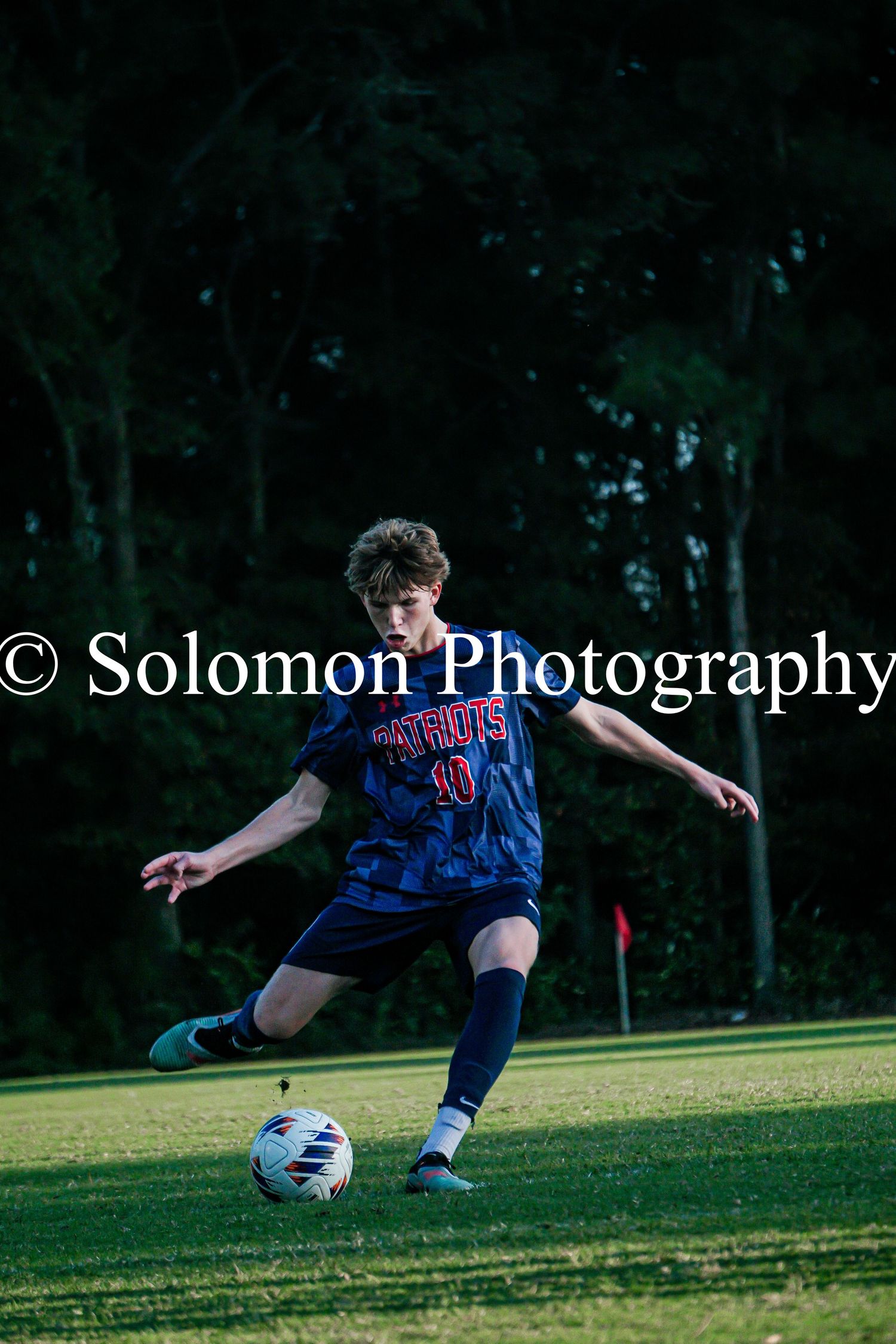Soccer player in Patriots jersey #10 kicks ball on green field during match.