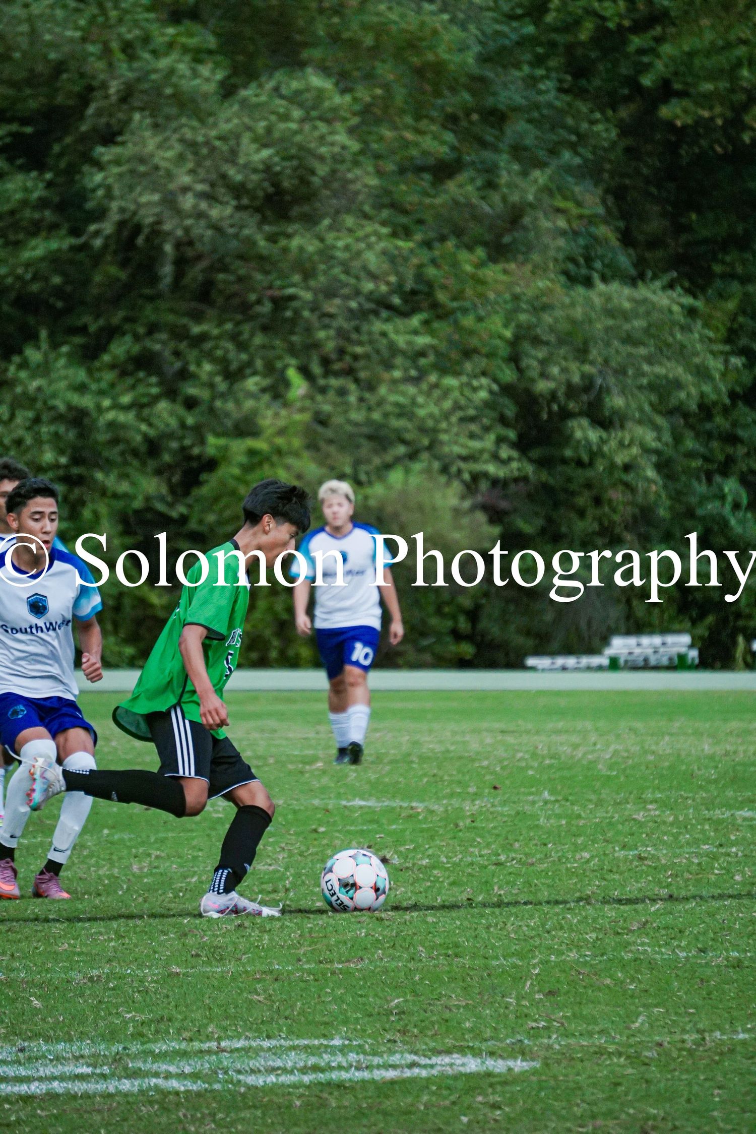 Youth soccer players battle for possession during competitive match on green field.