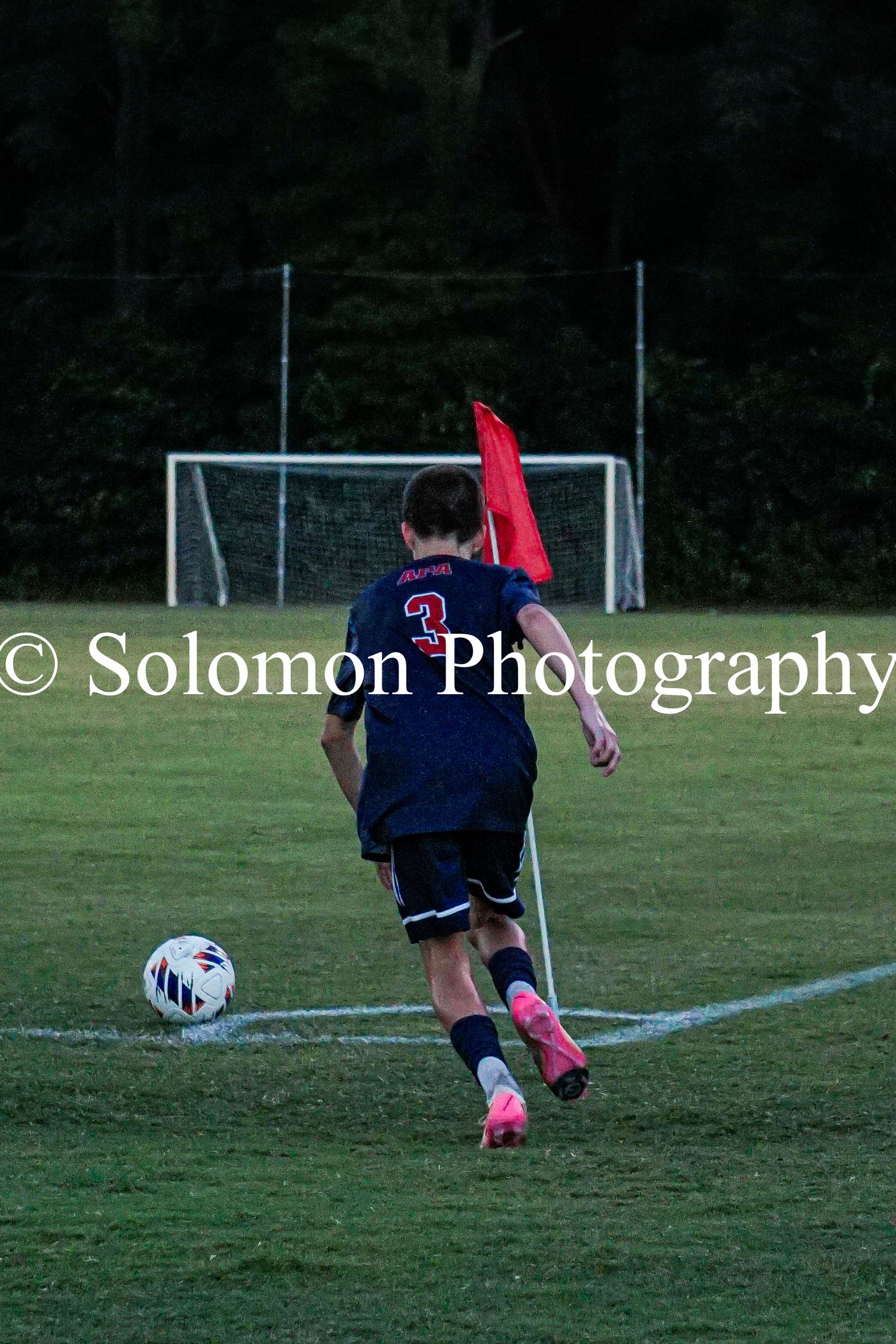 Soccer player in Patriots #3 jersey takes corner kick near red flag.