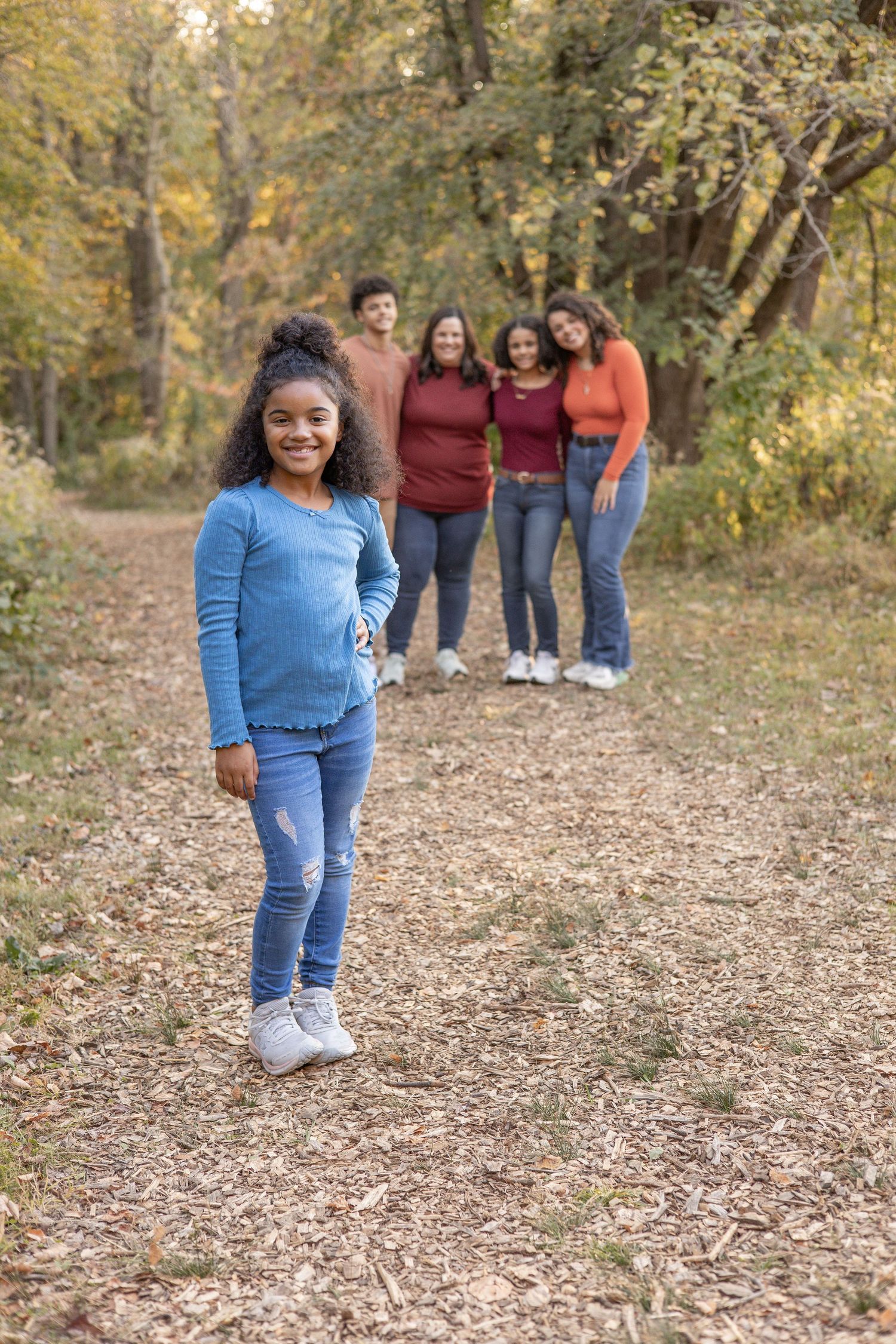 Springfield, IL family photographer captures a girl standing in the foreground with her family behind during a photo session in Central, IL