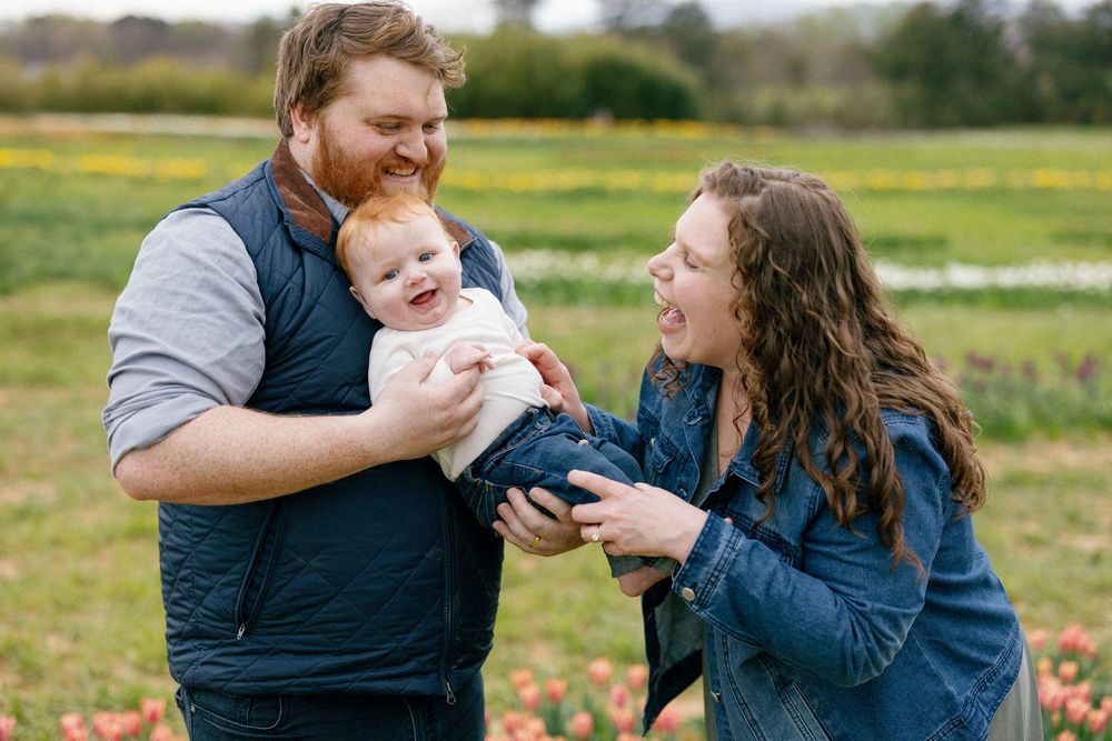A family enjoys a playful moment together in a sunny field with golden grass in the background.