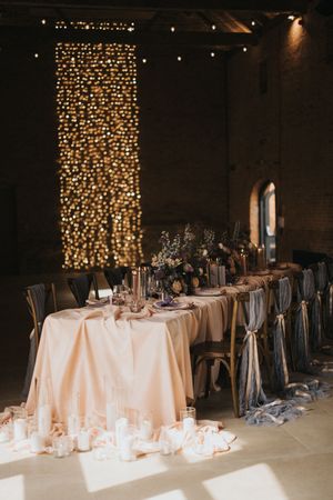 Elegant wedding reception tables with white linens and gray chair sashes set against a backdrop of cascading string lights.