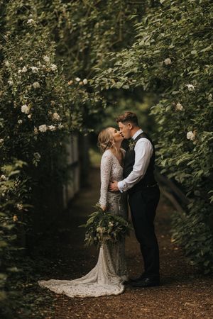 A romantic wedding couple shares an intimate moment together in a lush garden setting with dappled sunlight.