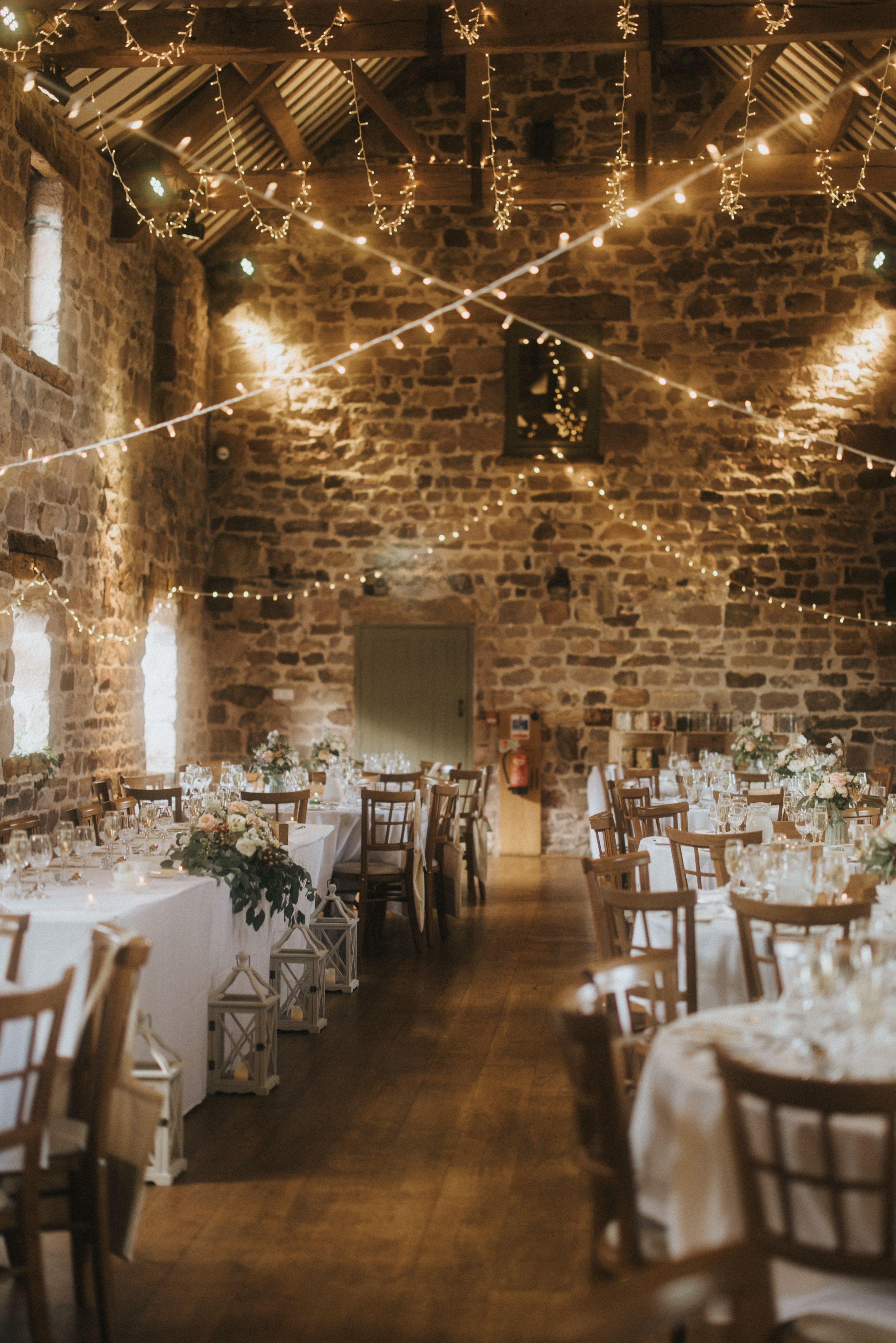Rustic wedding reception venue with exposed brick walls, twinkle lights, and elegant table settings in warm lighting.