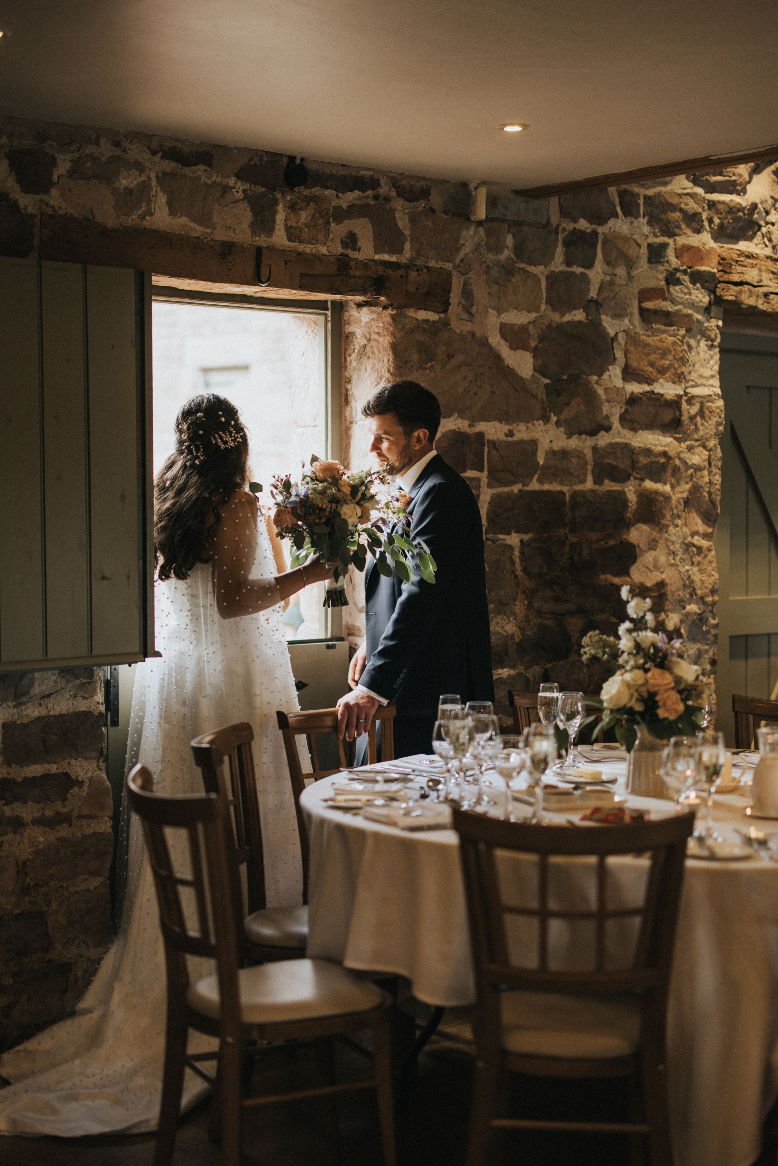 Rustic stone wall dining room with elegant table settings and natural light streaming through windows at a small venue.