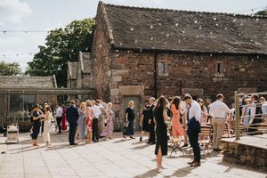 Guests gather outside a rustic brick barn venue during a summer wedding celebration.