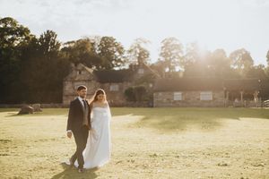 Newlywed couple walks through a sun-drenched meadow during golden hour as their special day comes to a close.