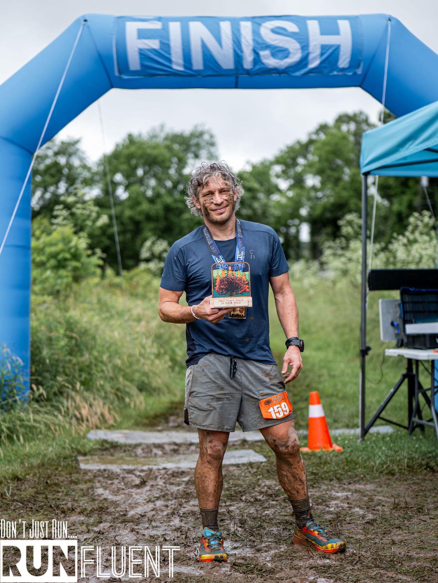 Runner celebrates while crossing finish line on wooded trail during outdoor race event.