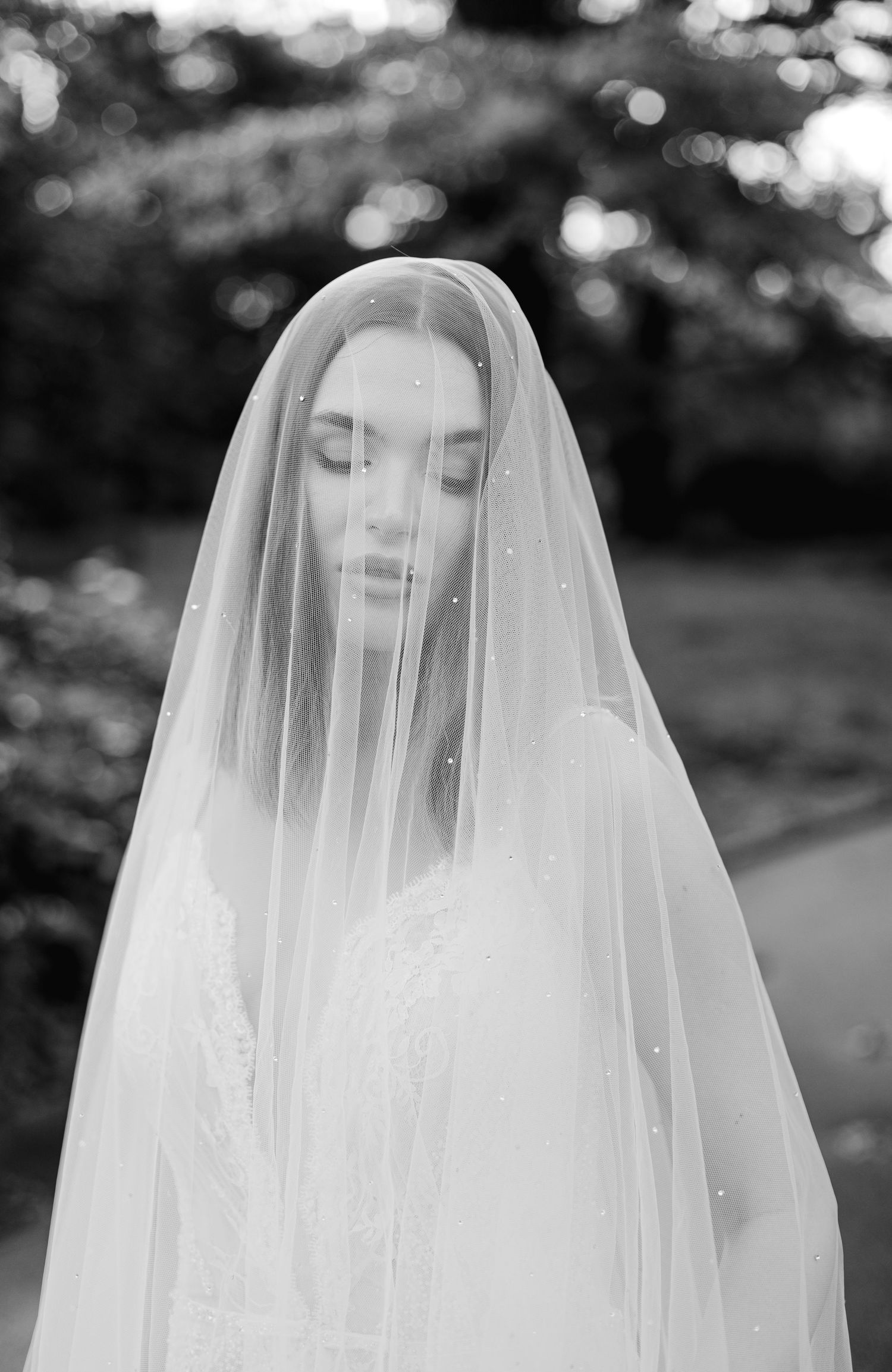 An ethereal black and white portrait of a bride wearing a delicate tulle veil in a garden setting.