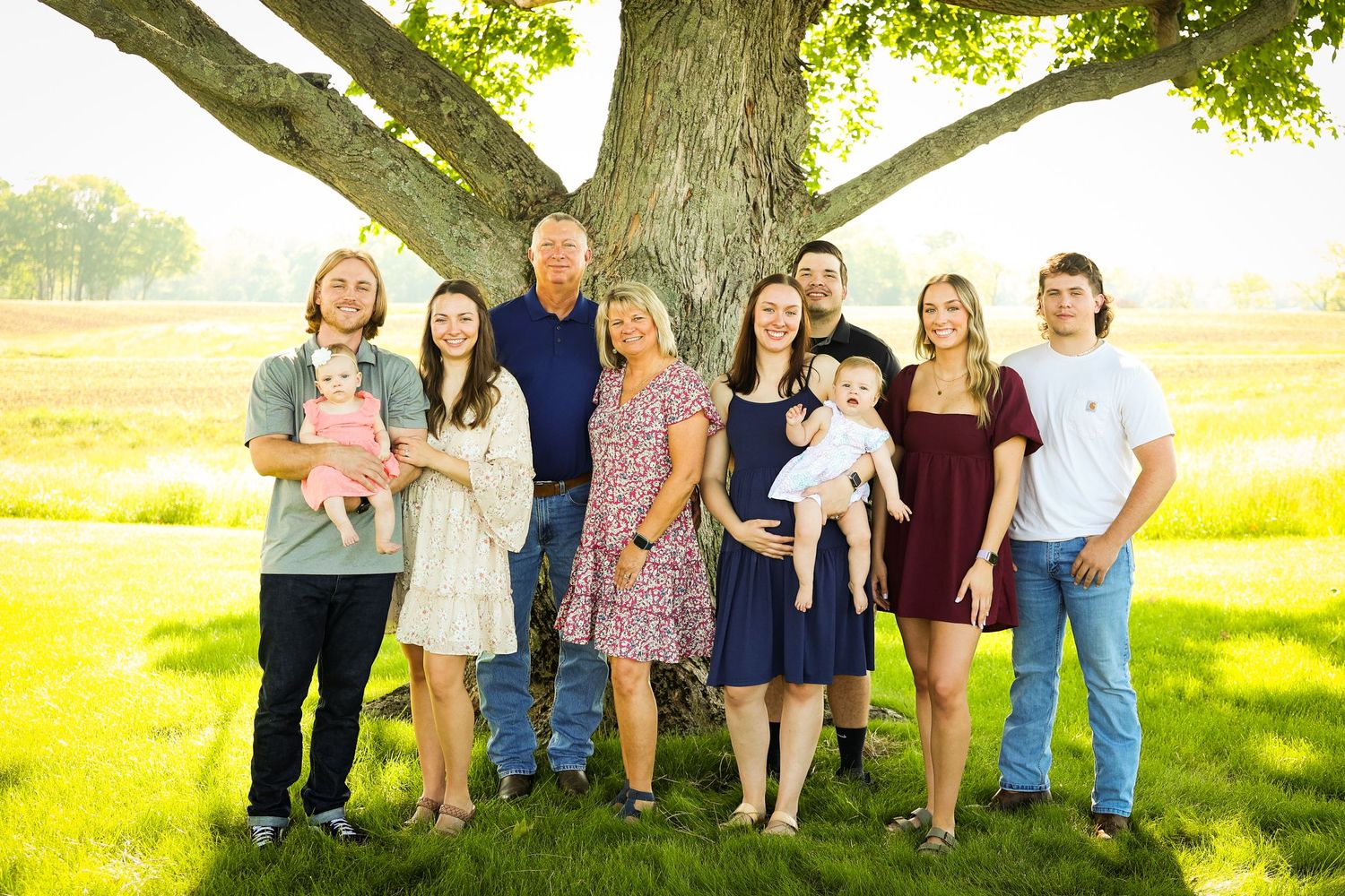 A group of people stand together on a grassy lawn during golden hour with long shadows cast across the ground.