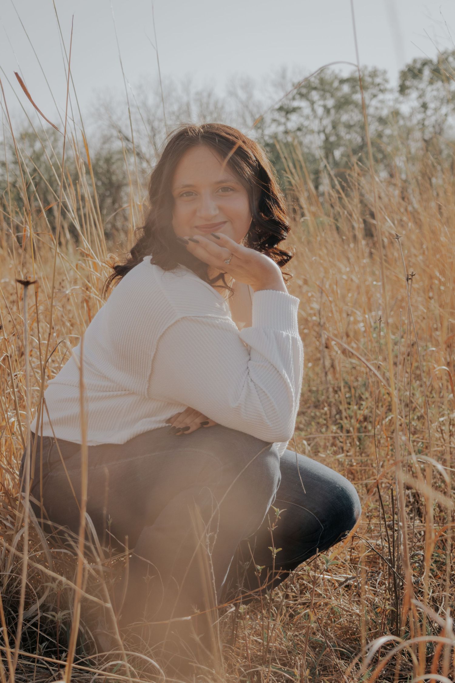 Portrait in a field of tall brown grasses during golden hour with a white sweater and dark pants.
