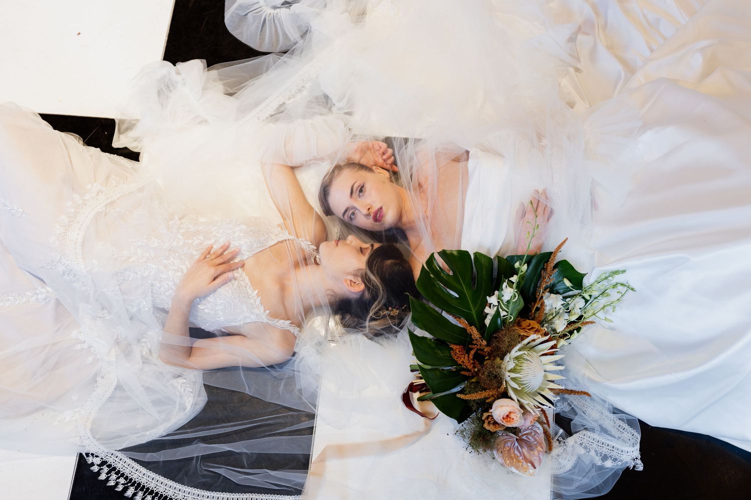 Aerial view shows someone in a white wedding dress lying on floor holding tropical flower bouquet and white veil.