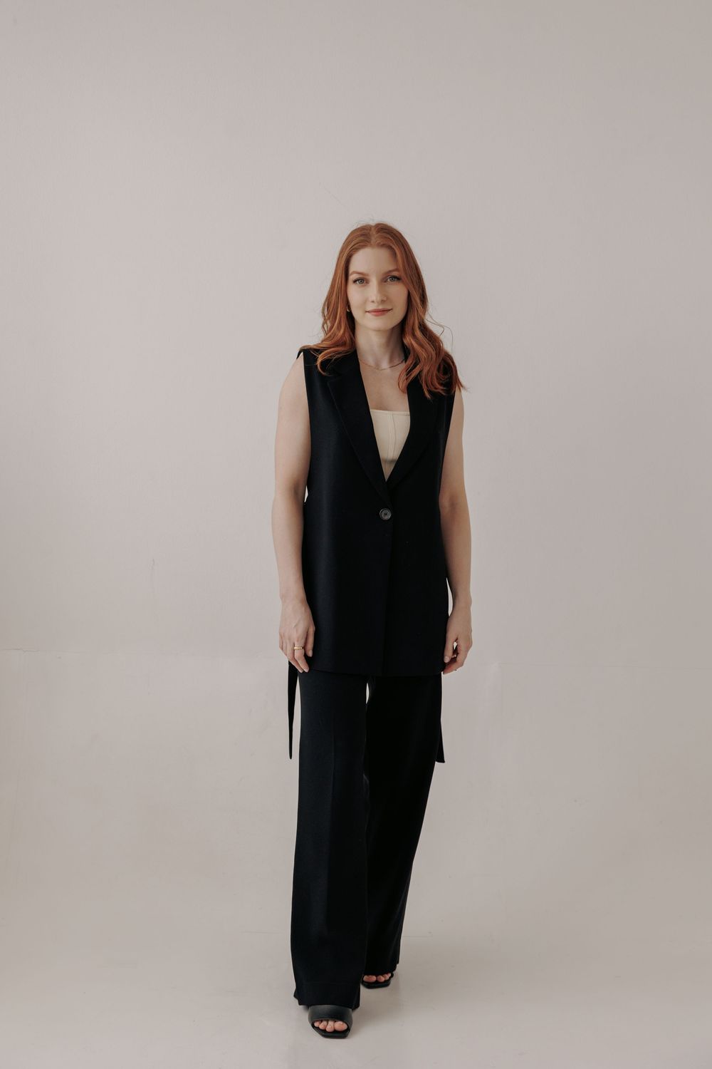 A series of fashion photos showing a minimalist black sleeveless suit vest dress against a neutral gray backdrop.