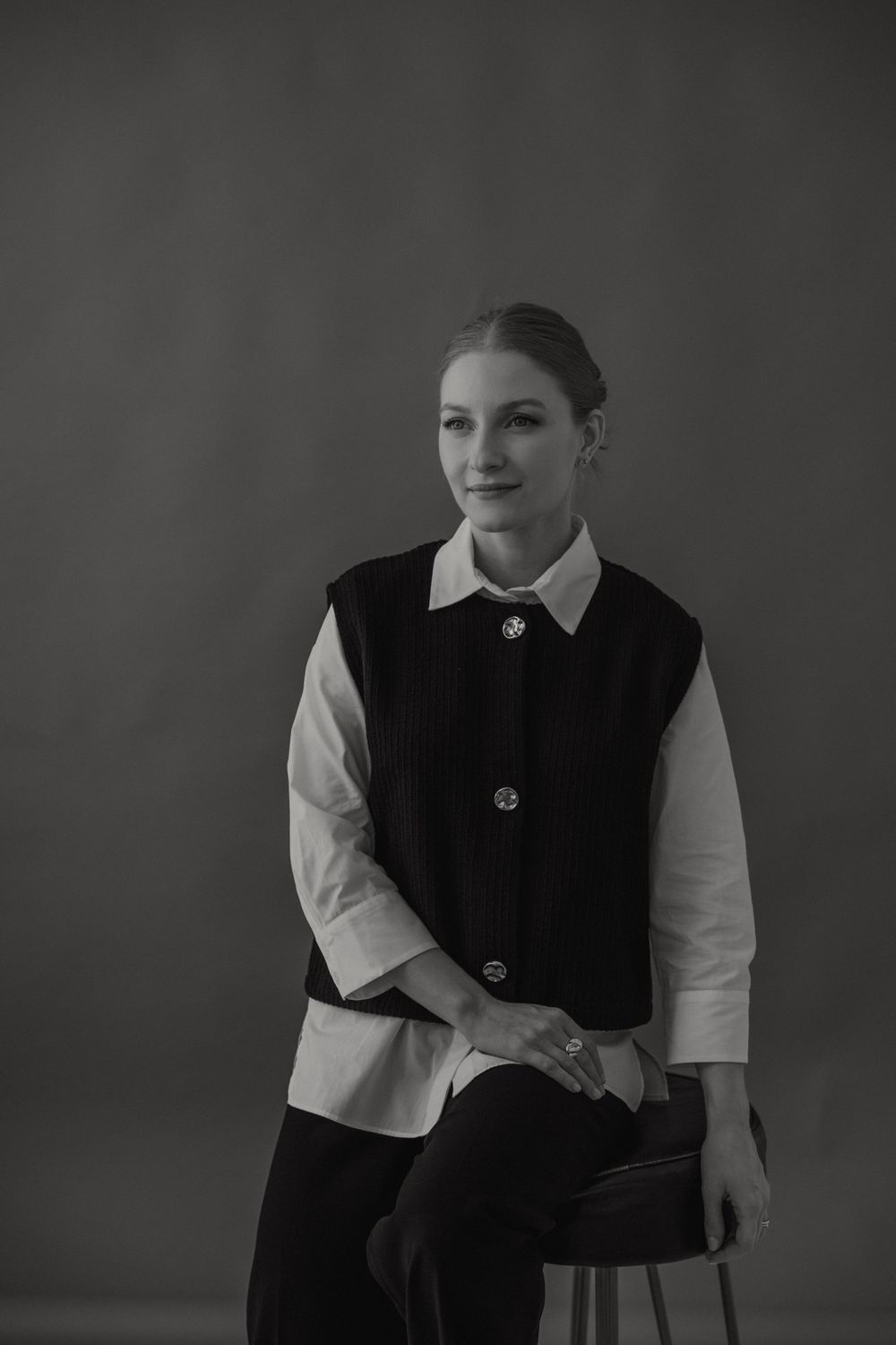 A figure in black vest and white shirt stands against a dark backdrop creating a dramatic portrait in low light.