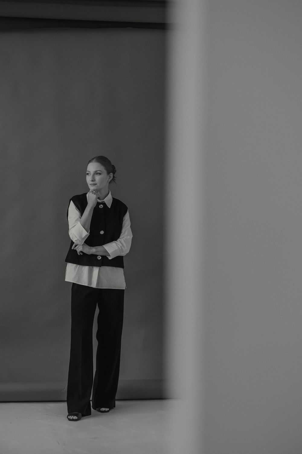 A figure in black and white clothing leans against a pole in a minimalist setting creating dramatic angles.