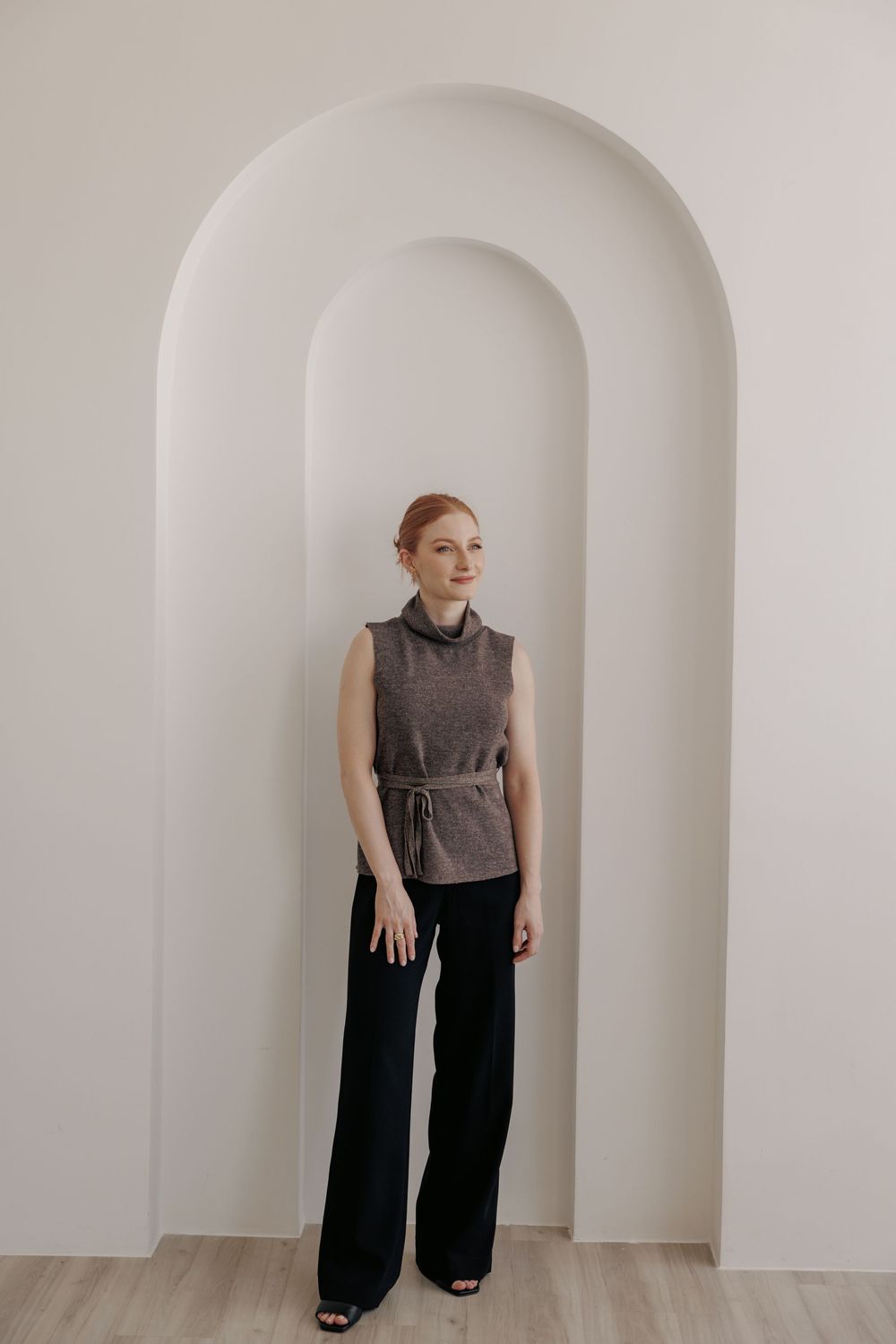 Gray sleeveless top and wide-leg black pants create a minimalist silhouette against white arched doorways.