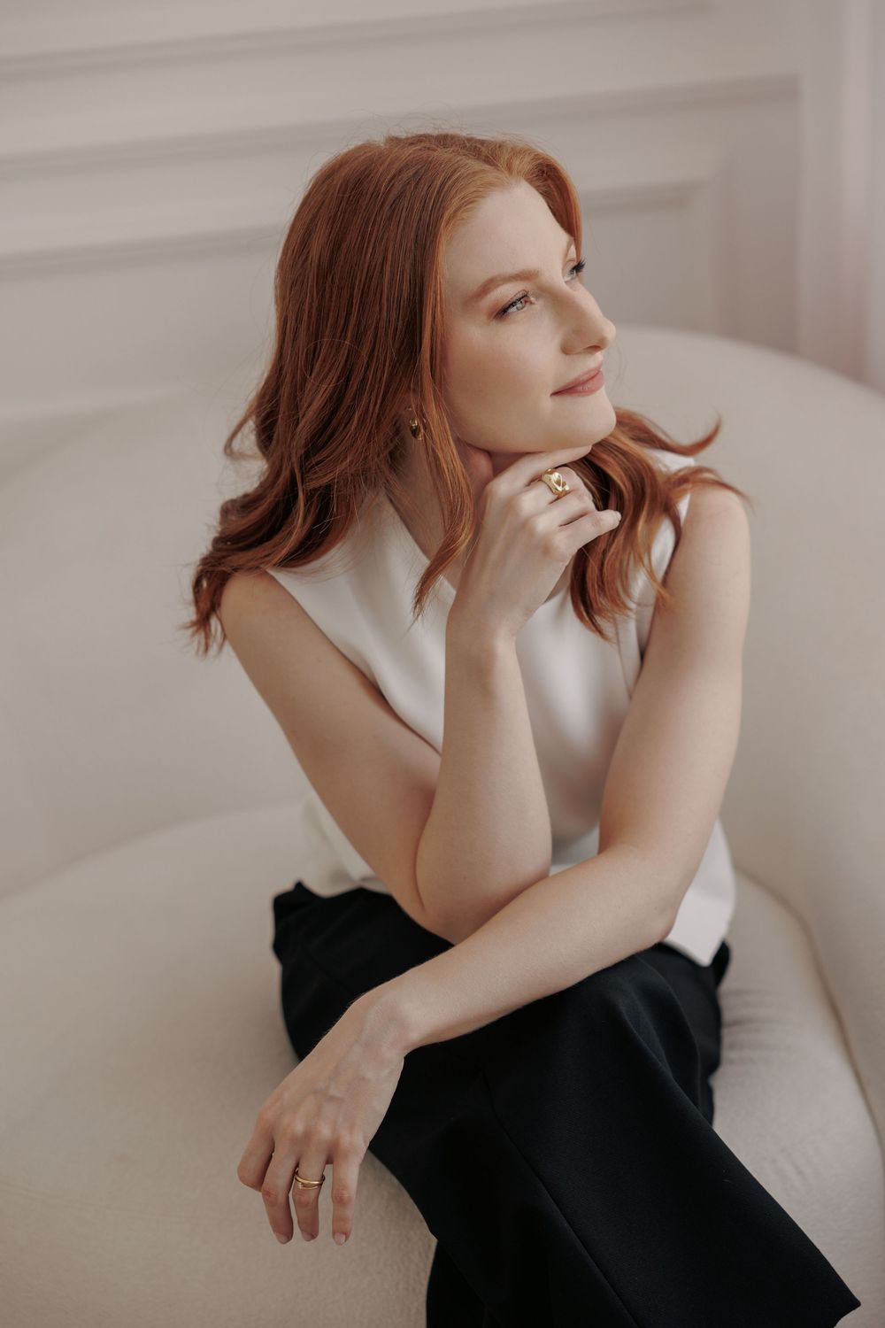 A figure in a black top sits contemplatively against a light background in an artistic portrait series.