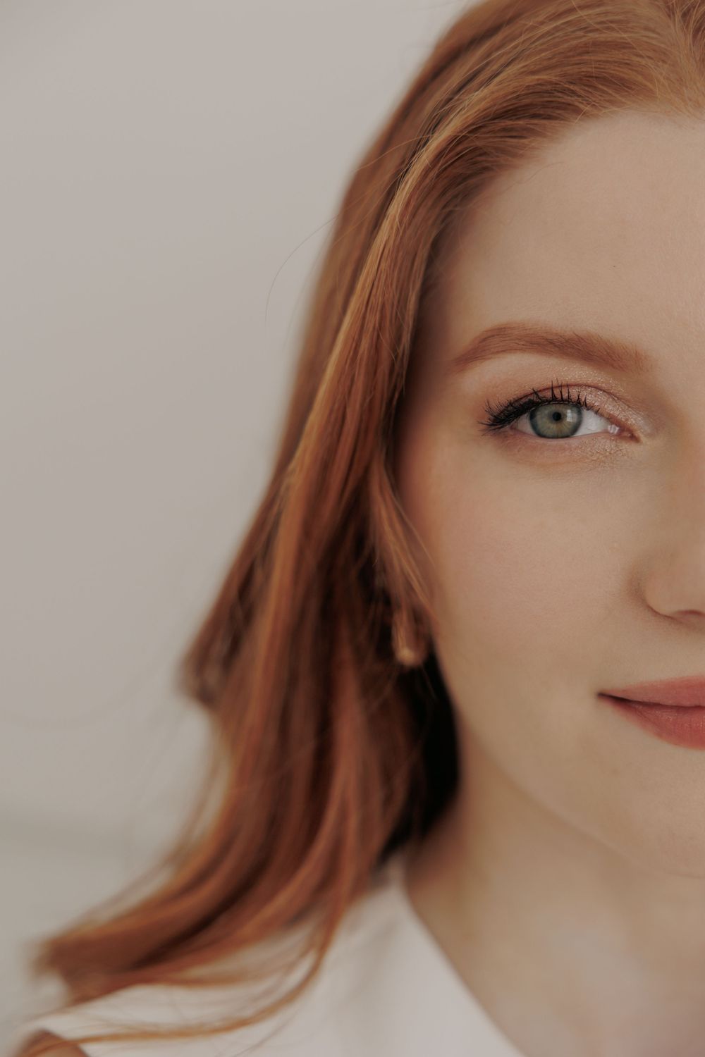 Close-up portrait with auburn hair and bright blue eyes against a light background.