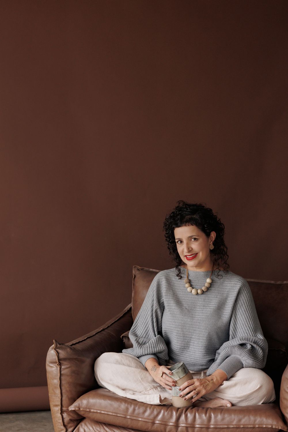 Person in gray sweater lounging comfortably on brown leather sofa in moody interior setting.