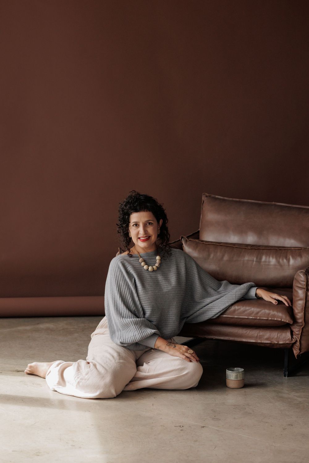 Person in casual grey sweater and white pants lounges on a brown leather sofa in an artistic photo series.