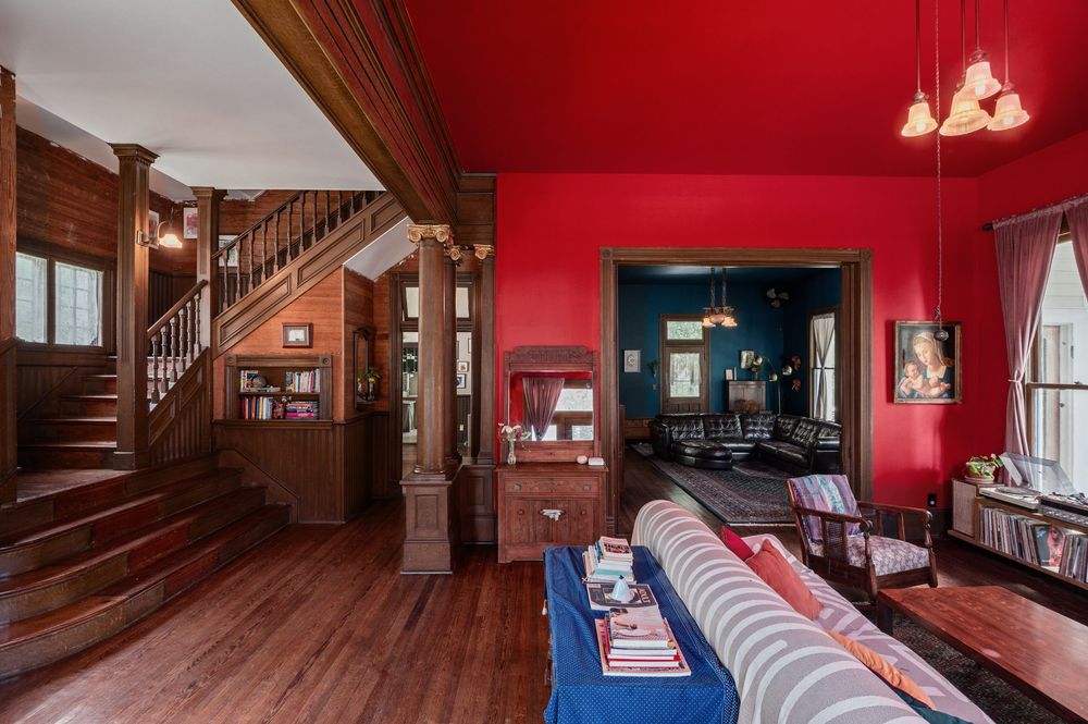 Living room interior with hardwood floors, red accent walls, and wooden staircase featuring traditional decor elements.