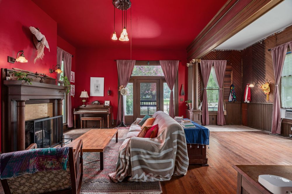 Vintage living room features deep red walls, ornate fireplace, and period furniture in a historic Victorian home interior.