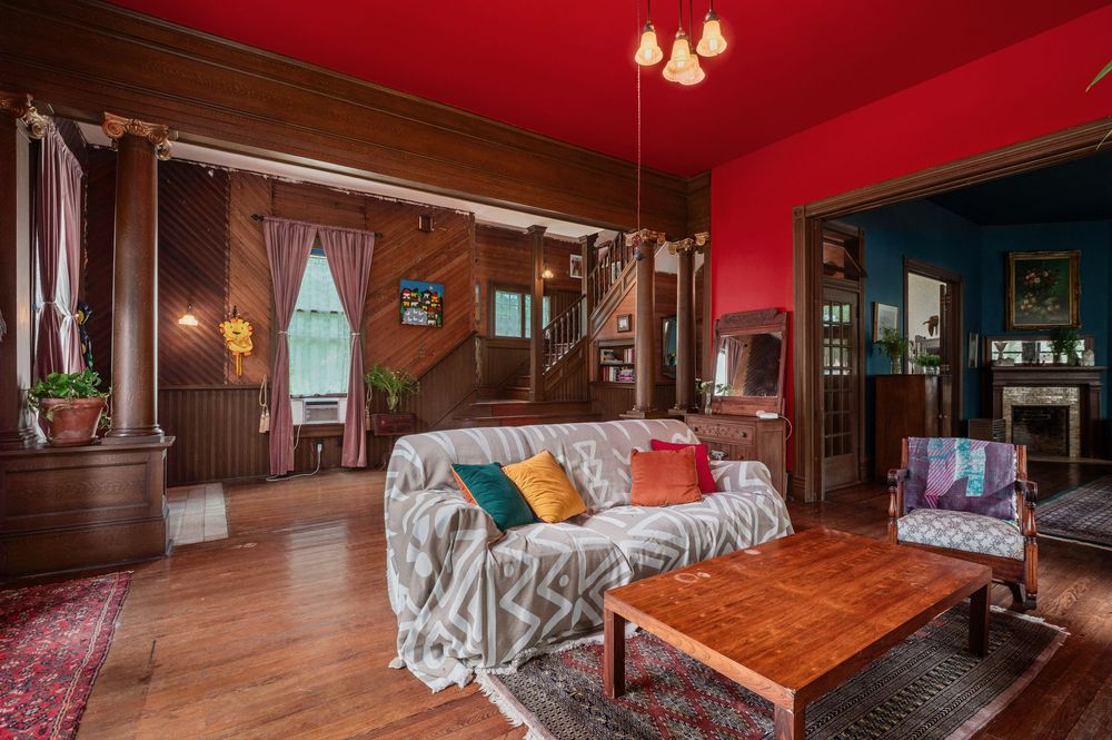 Cozy vintage living room with red walls, wooden paneling, daytime seating, and period furniture arranged around a coffee table.