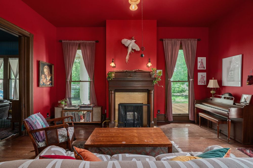 Spacious red-walled room with hardwood floors, antique furniture, and large windows letting in natural light.