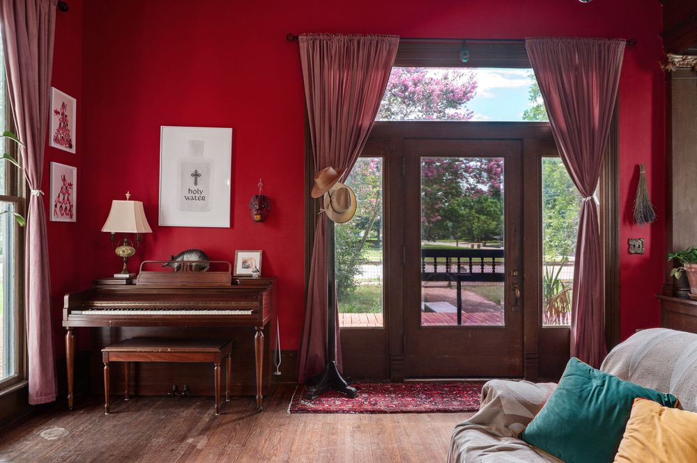 Panoramic view of a red living room with vintage furniture, wood trim, and large windows providing natural light.