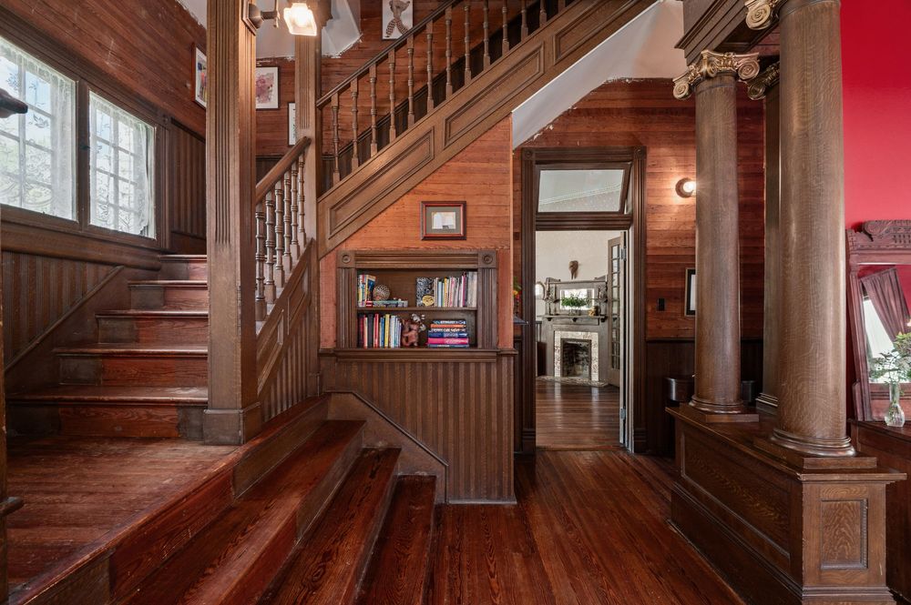 Interior view of wooden staircase and hardwood floors in craftsman style home with built-in shelving and red accent wall.