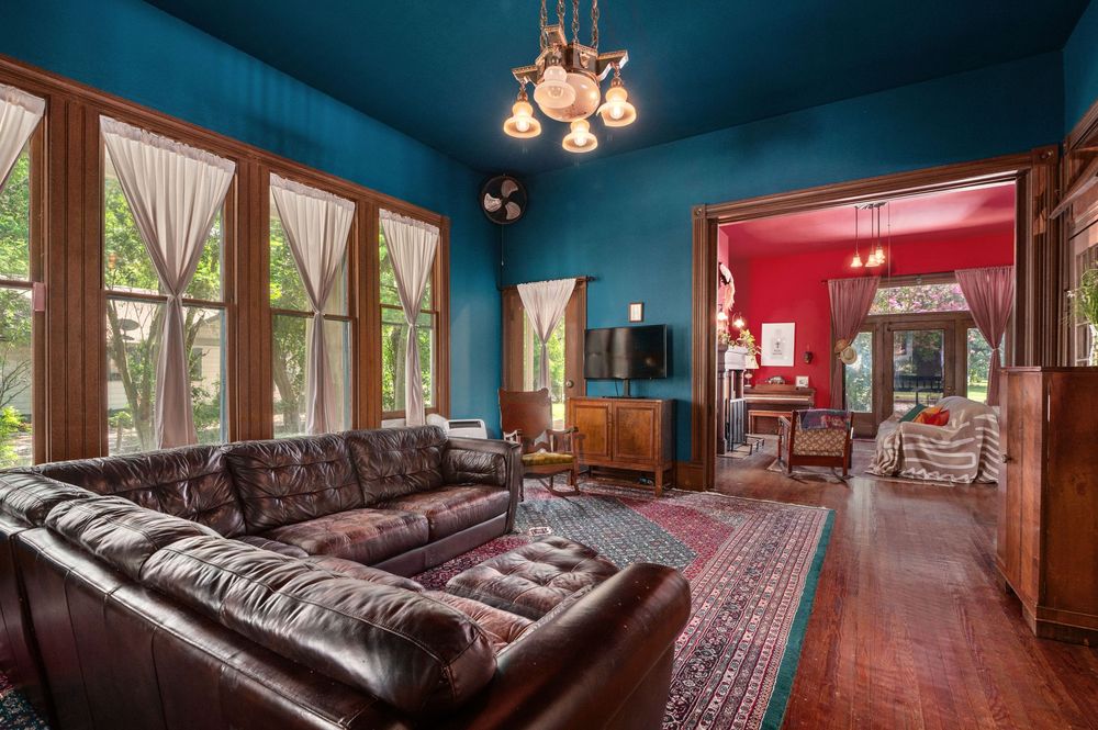 Spacious blue entertainment room with leather couches, chandelier lighting, and hardwood floors.