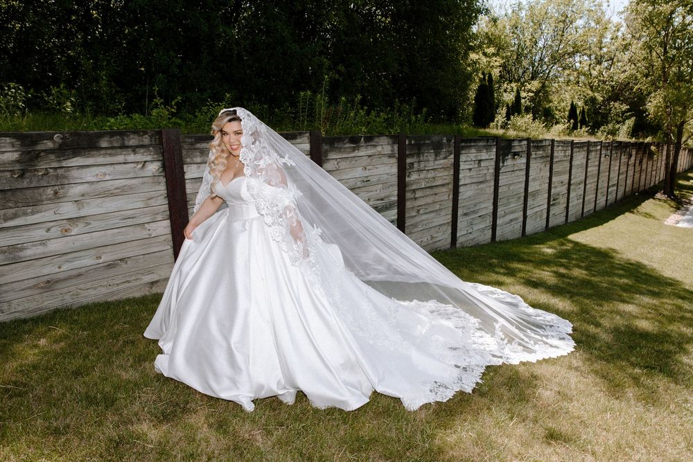 A dramatic flowing white wedding gown and long veil captured in an outdoor garden setting.