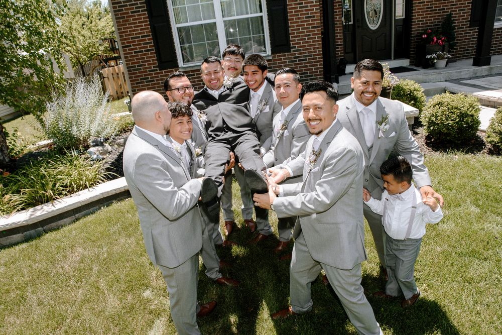 Groomsmen in gray suits pose playfully together on the lawn of an elegant white venue.