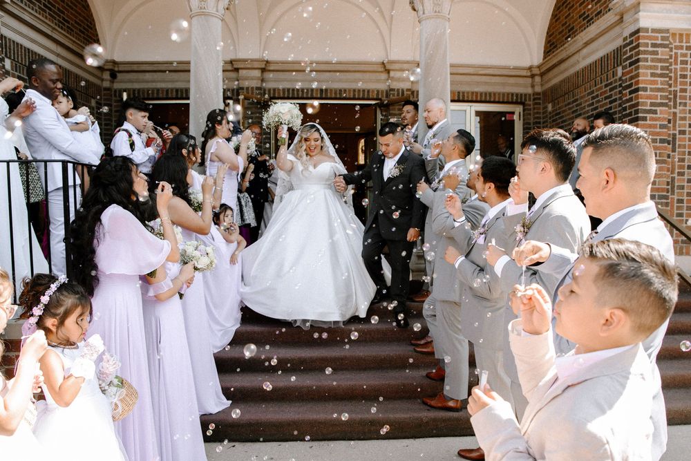 Wedding attendees in elegant white attire line up on grand steps of a brick building during celebration.