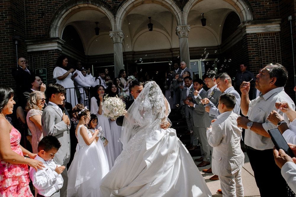 Wedding celebration with confetti shower under classical brick columned architecture.