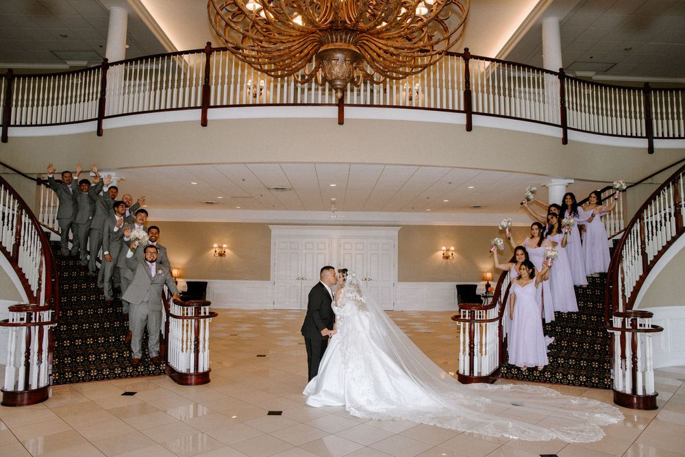 Wedding celebration in an elegant ballroom with chandelier and cascading staircase.
