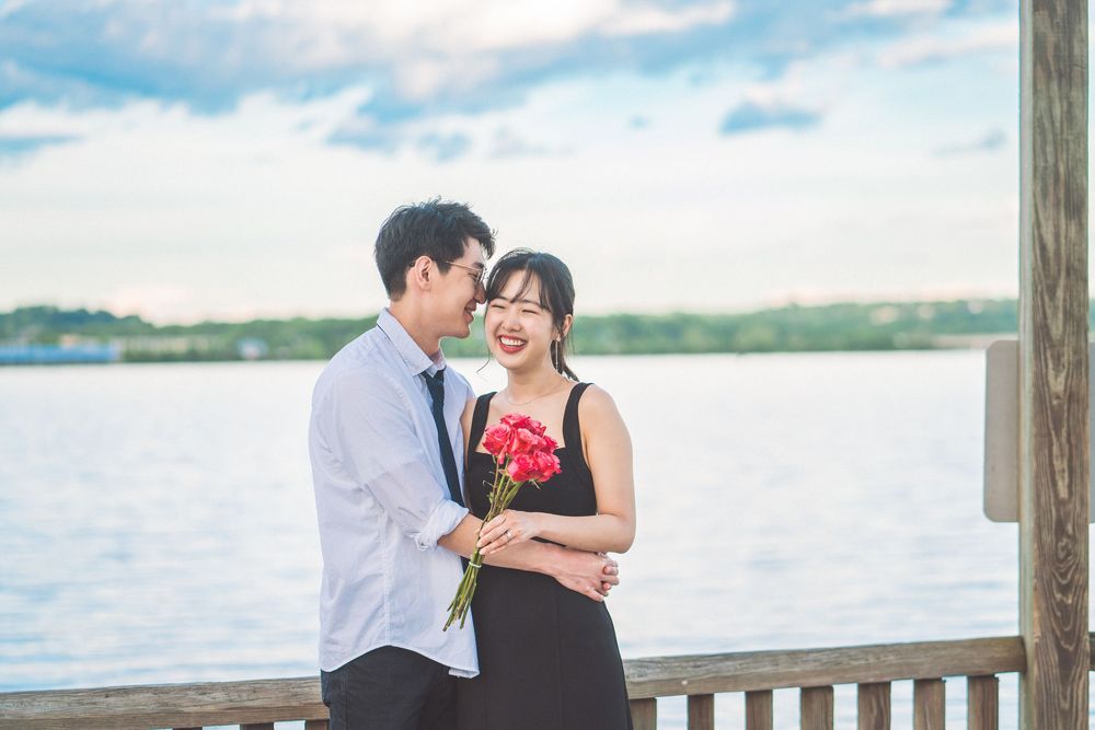 A couple shares romantic moments on a wooden pier overlooking a lake during a sunny day.