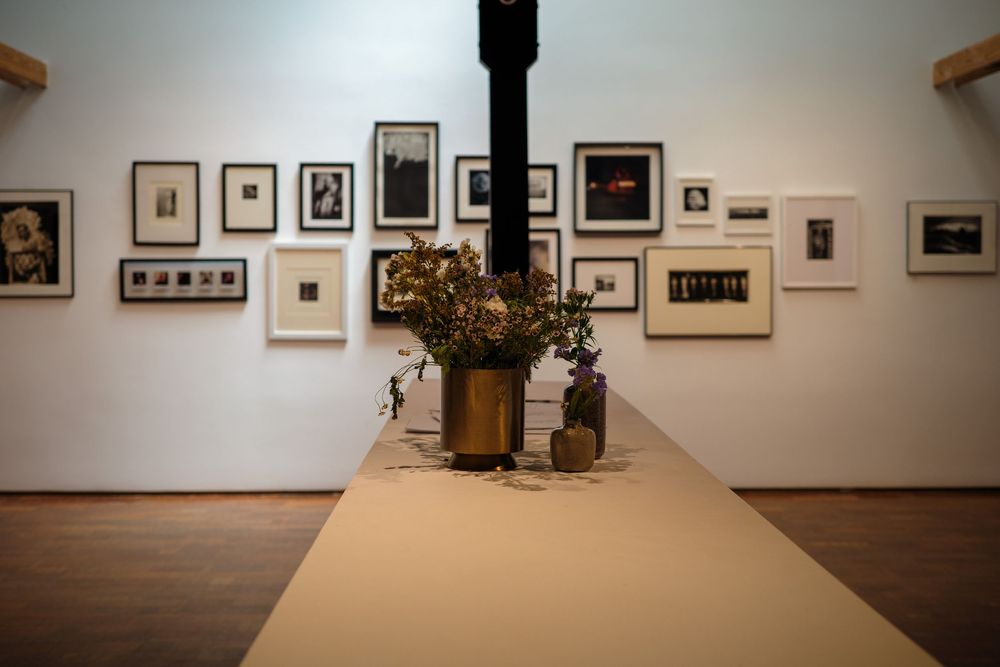 Art gallery interior with framed photographs on white walls and floral arrangement on a long table.